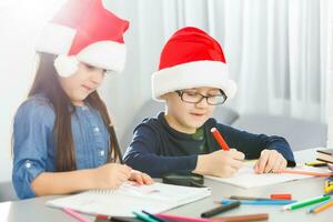 Writing letter to santa. Children in santa hats make wish list of presents for christmas. Winter holidays. Boy and girl, brother and sister draw photo