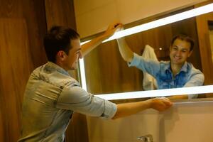 Man installing a mirror on wall in his renewed bathroom photo