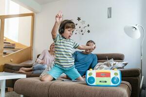 emocionado chico escuchando a música con auriculares en sofá a hogar con padres en antecedentes foto