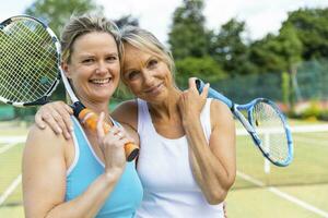 Portrait of two happy mature women on grass court at tennis club photo