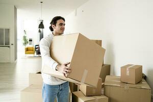 Smiling young man carrying cardboard box while moving in new apartment photo