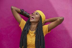 Portrait of woman with long dreadlocks laughing in front of a pink wall photo