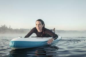 mujer acostado en inflable cenar paddleboard en lago iglesia, malo toelz, baviera, Alemania foto