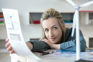 Portrait of woman leaning on desk in office with paper and wind turbine model photo