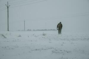 Silhouette of man with the metal detector who is searching on snow covered field during snow blizzard photo