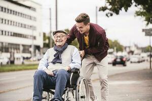 Young man pushing happy senior man in wheelchair photo