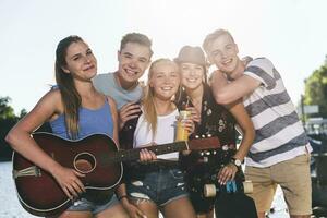 retrato de grupo de contento amigos con guitarra a el orilla foto