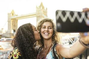 UK, London, two friends taking a selfie with Tower Bridge in background photo