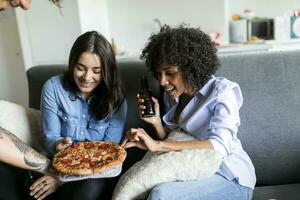 Tattooed man offering pizza to friends sitting on couch photo