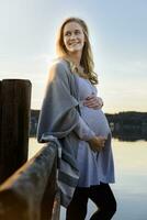 Smiling pregnant woman standing at lakeshore photo