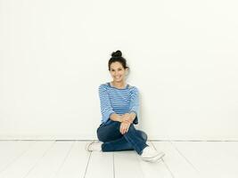 Beautiful young woman with black hair and blue white striped sweater sitting on the ground in front of white background photo