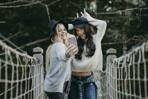 dos contento joven mujer en un suspensión puente tomando un selfie foto