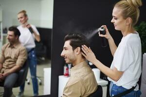 Smiling hairdresser using hairspray on man's hair photo