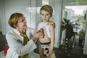 Doctor examining toddler boy with a stethoscope photo