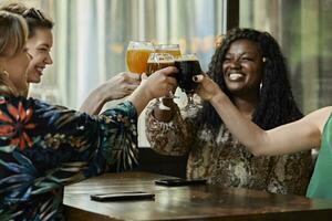 Happy female friends clinking craft beer glasses in a pub photo