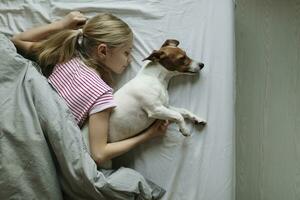 Blond girl lying on bed with her dog sleeping, top view photo