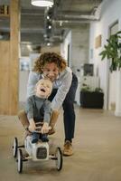 Businessman pushing son on toy car in office photo