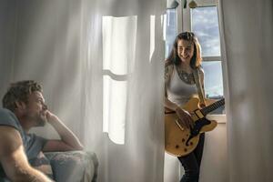 Man looking at young woman at the window at home with a guitar photo