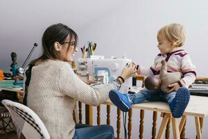 Happy mother with little daughter at home using sewing machine photo