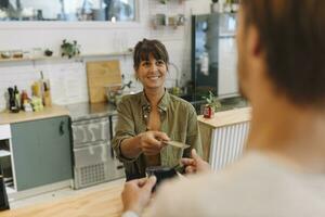 Smiling female owner giving back credit card to male customer at checkout in coffee shop photo