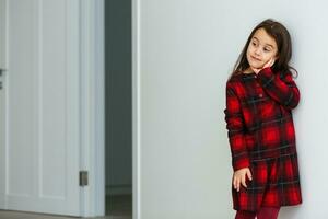 Beautiful little girl in skirt standing near white wall and posing like model photo