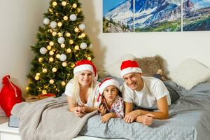 contento familia a hogar. madre, padre y niño acostado en el cama con Navidad regalo. invierno fiesta concepto foto
