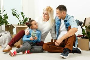 contento familia sentado en de madera piso. padre, madre y niño teniendo divertido juntos. Moviente casa día, nuevo hogar y diseño interior concepto foto