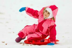 Cute little girl sliding down from the hill top covered with white and fluffy snow. One of the children favorite activity in winter time. photo