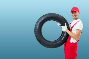 car mechanic carrying tire on blue background. happy man smiling amd looking into camera photo