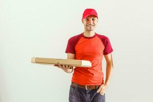 Photo of happy man from delivery service in red t-shirt and cap giving food order and holding boxes isolated over white background