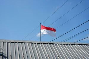 el rojo y blanco indonesio bandera es volador en contra un antecedentes de azul cielo y cables foto