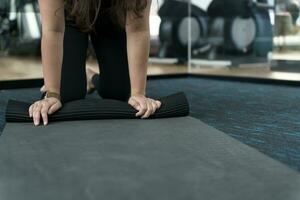 aptitud mujer plegable ejercicio estera antes de trabajando fuera en yoga estudio. laminación yoga estera después formación sano estilo de vida foto