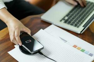 Charging mobile phone battery with wireless charging device in the table. Smartphone charging on a charging pad. Mobile phone near wireless charger Modern lifestyle technology concept photo