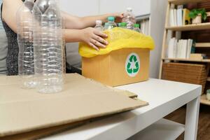 Home recycle eco green zero concept Woman throwing empty plastic bottle in recycling bin with yellow garbage bags at home. photo