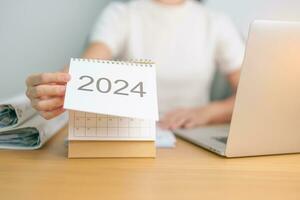 2024 año calendario en mesa con negocio mujer utilizando ordenador portátil computadora. cuenta regresiva, contento nuevo año, resolución, objetivos, plan, acción, misión y financiero concepto foto