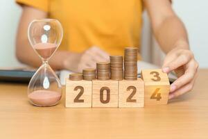 Happy New Year with sandglass and flipping 2023 change to 2024 block. Resolution, Goals, Plan, Action, Money Saving, Retirement fund, Pension, Investment and Financial concept photo