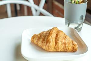 Croissant bread in a white plate lies on a white table photo