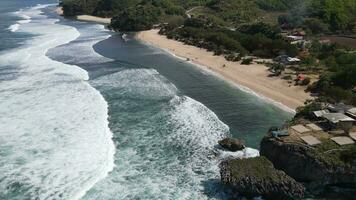 Aerial drone view of umbrellas, boats and people having holiday at the beach in Yogyakarta Indonesia video