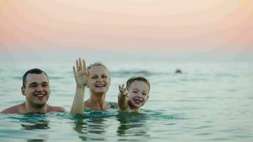 Family of three waving with hands from the sea video