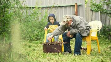 Grandson and grandfather sitting by fire in the yard video