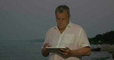 homme dactylographie sur tablette tandis que permanent sur plage video