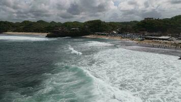 Aerial drone view of umbrellas, boats and people having holiday at the beach in Yogyakarta Indonesia video