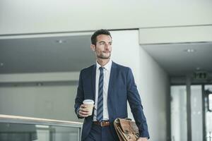 empresario con maletín caminando en oficina edificio, participación taza de café foto