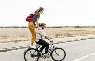 contento joven Pareja montando juntos en uno bicicleta en país la carretera foto