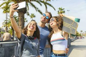 Tres juguetón amigos con patineta tomando un selfie foto