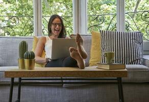 Cheerful woman using laptop while sitting on sofa in living room photo