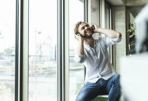 Happy casual young man listening to music with headphones at the window photo