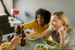 Happy girlfriends sitting at dining table clinking beer bottles photo
