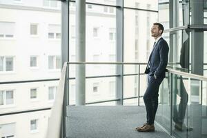 Successful businessman standing in office building, looking out of window, daydreaming photo