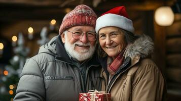 A Happy Senior Couple Holds A Wrapped Christmas Gift Outdoors in a light Snowfall. photo